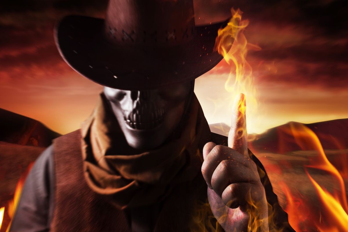 Photo of a demonic skull head cowboy in hat casting fire spell with his arm and finger on a sunset desert background.